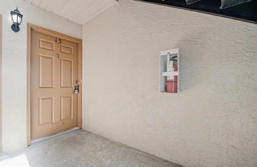 An exterior view of a tan apartment door numbered 13 with a wall-mounted fire extinguisher — 4613 GATE PLACE UNIT 104, ORLANDO, FL