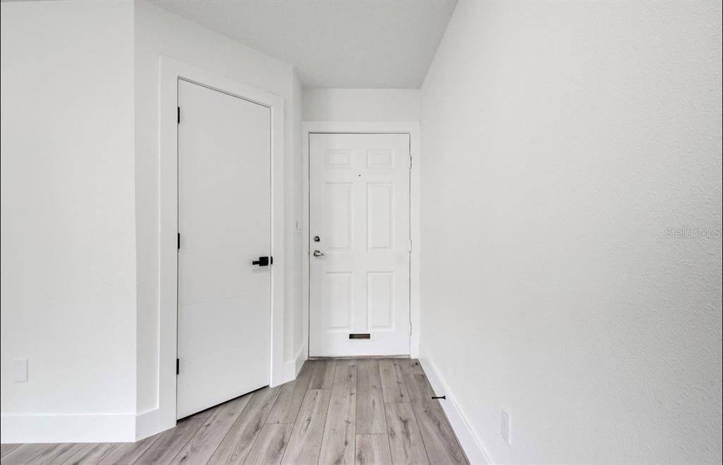 A hallway features white walls, gray wood-look flooring, a modern interior door, and an entry door — 4613 GATE PLACE UNIT 104, ORLANDO, FL