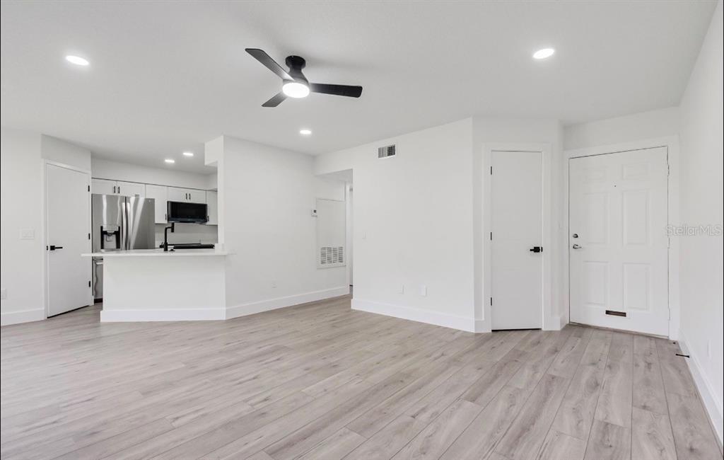 An open-concept living area features light wood-look flooring, white walls, and a kitchen with appliances — 4613 GATE PLACE UNIT 104, ORLANDO, FL