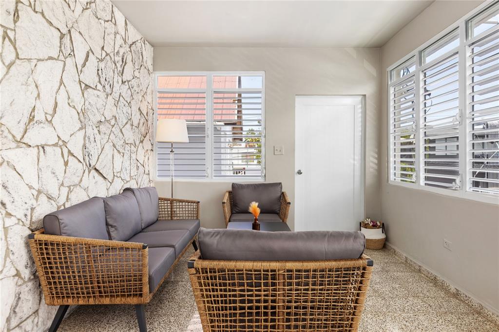 A sunroom features a stone accent wall, wicker furniture, and large windows with white shutters — 56 MARÍA MOCZO UNIT 2, SAN JUAN, PR