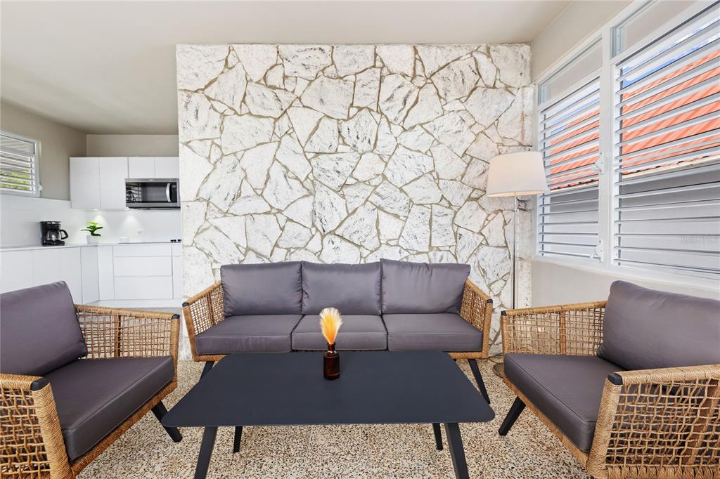 A living area features a stone accent wall, wicker furniture, and an adjacent white kitchen — 56 MARÍA MOCZO UNIT 2, SAN JUAN, PR