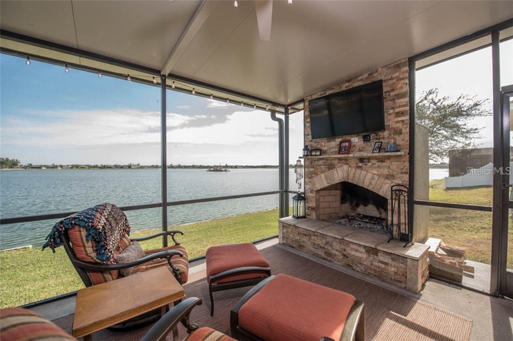 A screened-in patio features a stone fireplace, a television, and a view of the water — 1742 MIRA LAGO CIRCLE, RUSKIN, FL