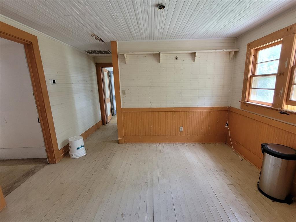 An empty room features white beadboard walls, wood wainscoting, and light-colored wood flooring — 801 NE 1ST STREET, MICANOPY, FL