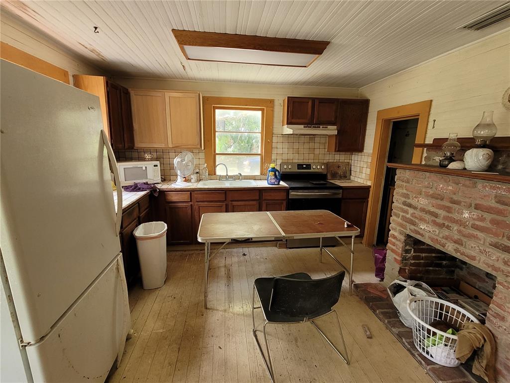 A kitchen with wood cabinets, a brick fireplace, and a folding table on wood floors — 801 NE 1ST STREET, MICANOPY, FL