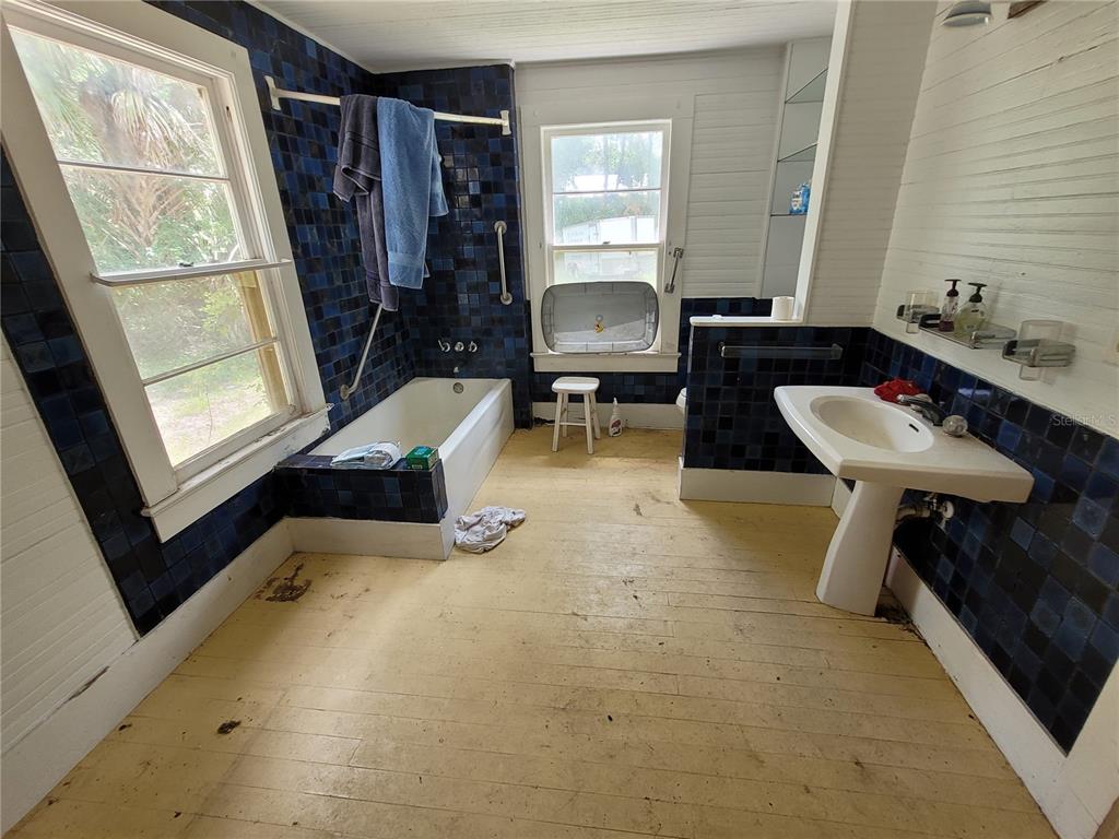 A bathroom features blue tiled walls, a pedestal sink, a bathtub, and wood flooring — 801 NE 1ST STREET, MICANOPY, FL