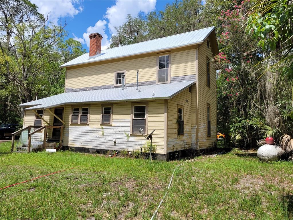 A two-story yellow wood-sided house with a metal roof and a brick chimney — 801 NE 1ST STREET, MICANOPY, FL