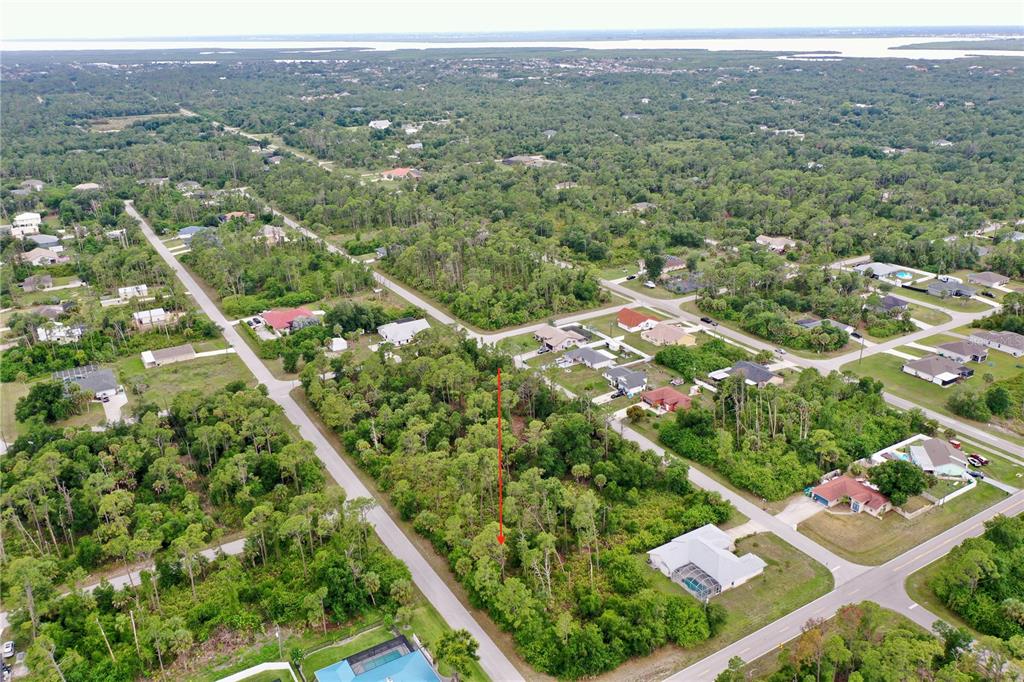 An aerial view shows a vacant, wooded residential lot marked by a red arrow — 3019 SUDBURY STREET, PORT CHARLOTTE, FL