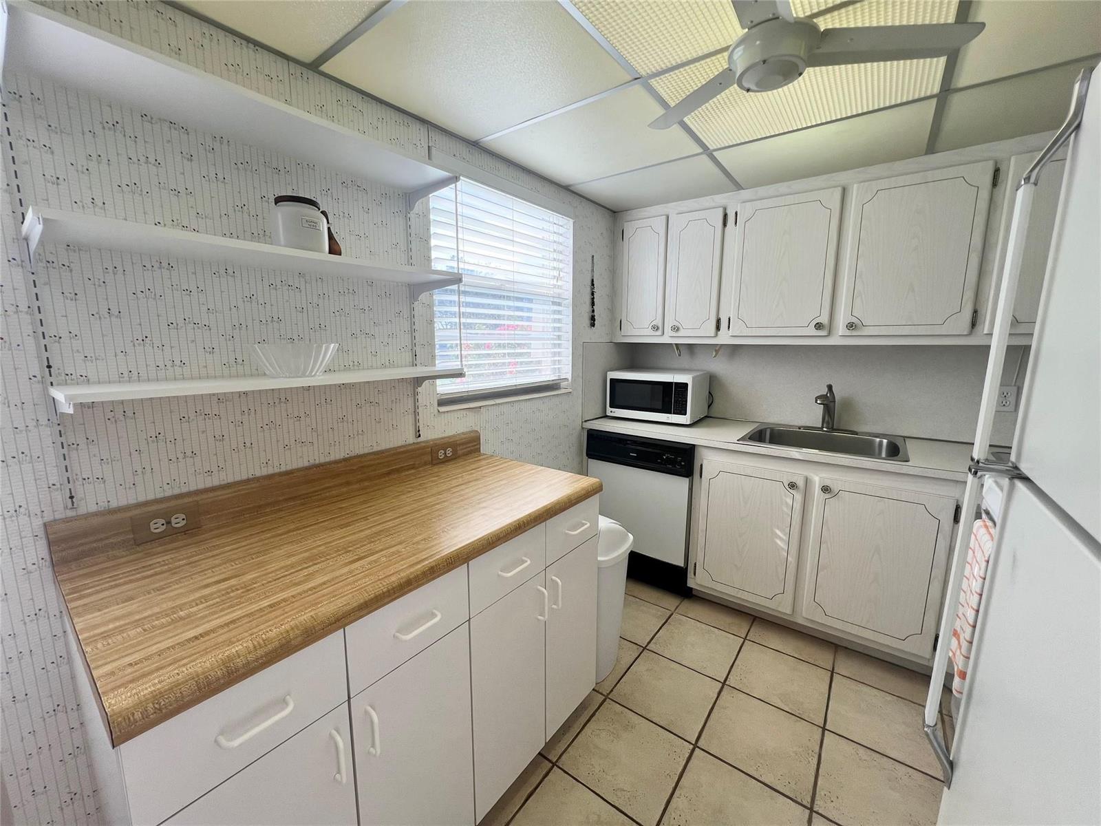 A kitchen features white cabinets, wood-look laminate countertops, open shelving, and a tiled floor — 244 Farnham K # 244, Deerfield Beach FL 33442, DEERFIELD BEACH, FL
