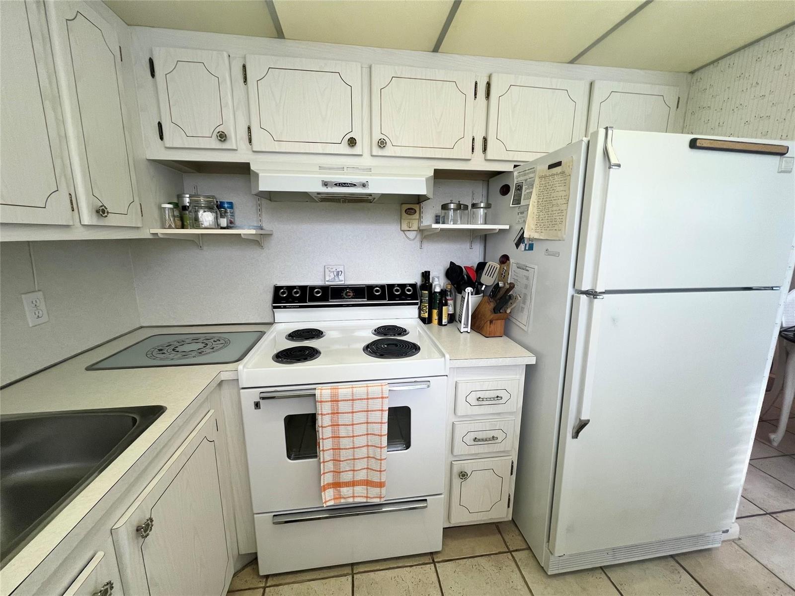 A kitchen features white cabinets, a white stove, a refrigerator, and light-colored tile flooring — 244 Farnham K # 244, Deerfield Beach FL 33442, DEERFIELD BEACH, FL