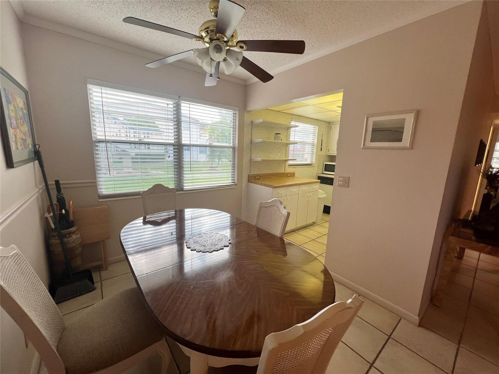 A dining area with a wooden table, ceiling fan, and an adjacent kitchen pass-through — 244 Farnham K # 244, Deerfield Beach FL 33442, DEERFIELD BEACH, FL