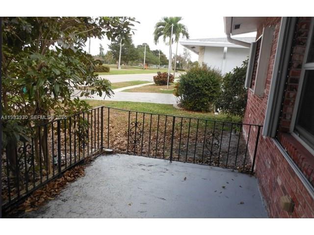 A concrete patio with a black metal railing overlooks a grassy yard and street — 7540 Margate Blvd, Margate FL 33063, MARGATE, FL