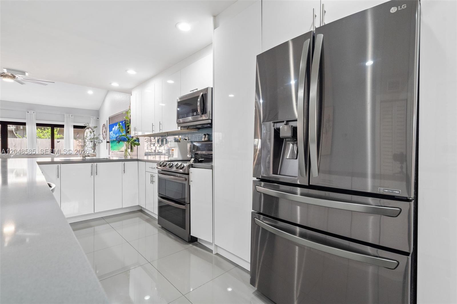 A modern kitchen features white cabinetry, stainless steel appliances, and glossy tile flooring — 1946 SW 81st Ter, Davie FL 33324, DAVIE, FL