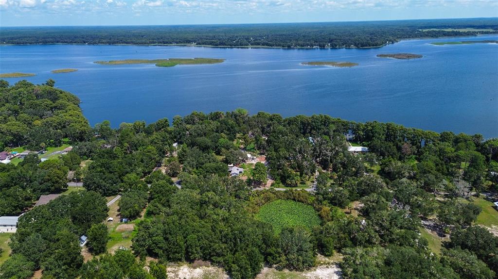 An aerial view shows a wooded property with several buildings situated along a large lake — 8601 W BASS LAKE ROAD UNIT 12, CRYSTAL RIVER, FL