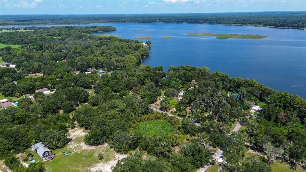 An aerial view shows a wooded residential area bordering a large lake under a blue sky — 8601 W BASS LAKE ROAD UNIT 12, CRYSTAL RIVER, FL