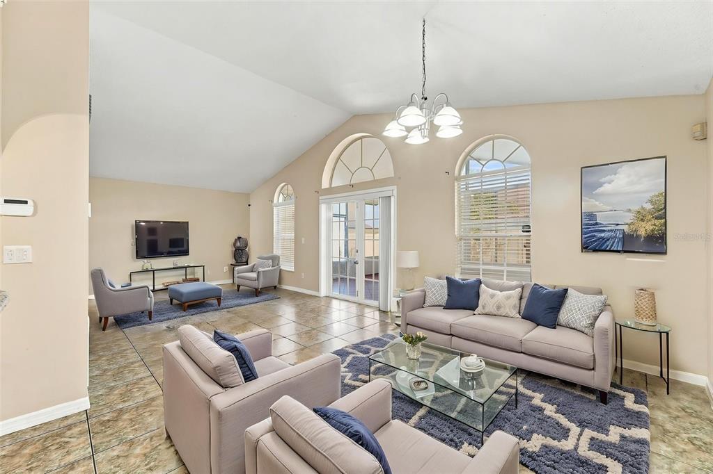 A living room with vaulted ceilings, tile floors, a glass coffee table, and large windows — 2411 PARSONS POND CIRCLE, KISSIMMEE, FL