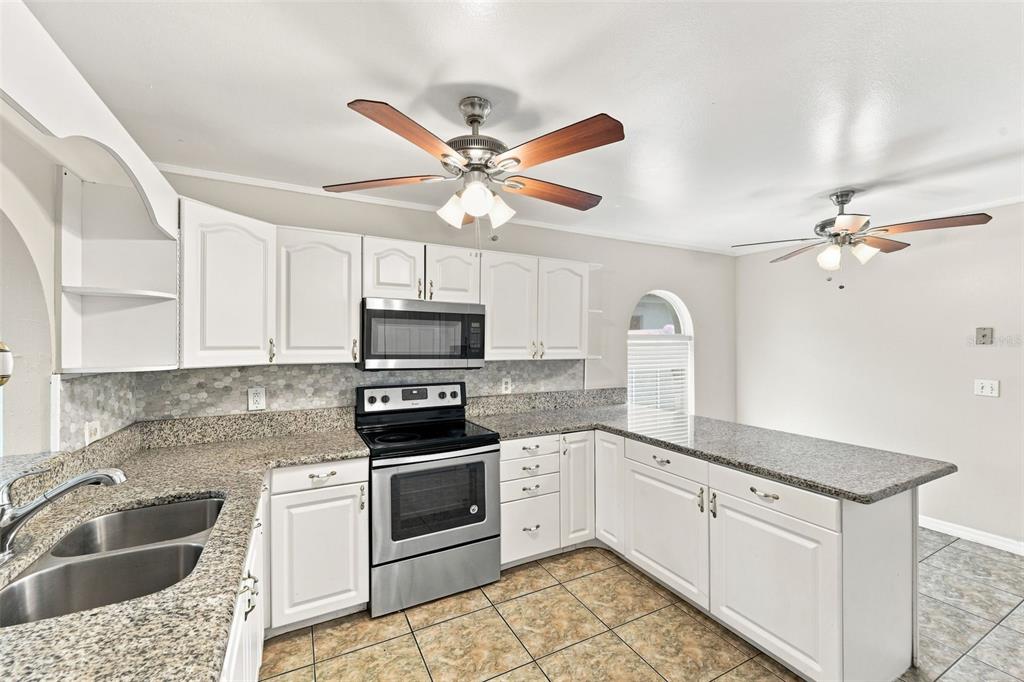A kitchen with white cabinets, granite countertops, stainless steel appliances, and two ceiling fans — 2411 PARSONS POND CIRCLE, KISSIMMEE, FL