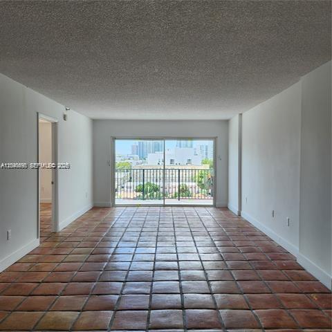 An empty room with terracotta tile flooring and a sliding glass door leading to a balcony — 1345 West Ave # 702, Miami Beach FL 33139, MIAMI BEACH, FL