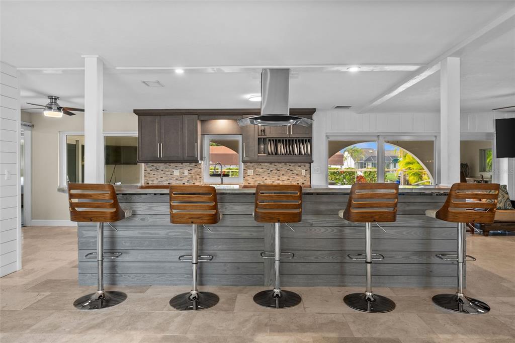 A kitchen island with five wooden bar stools faces a sink and stainless steel range hood — 2129 W TOBAGO CIRCLE, FORT MYERS, FL