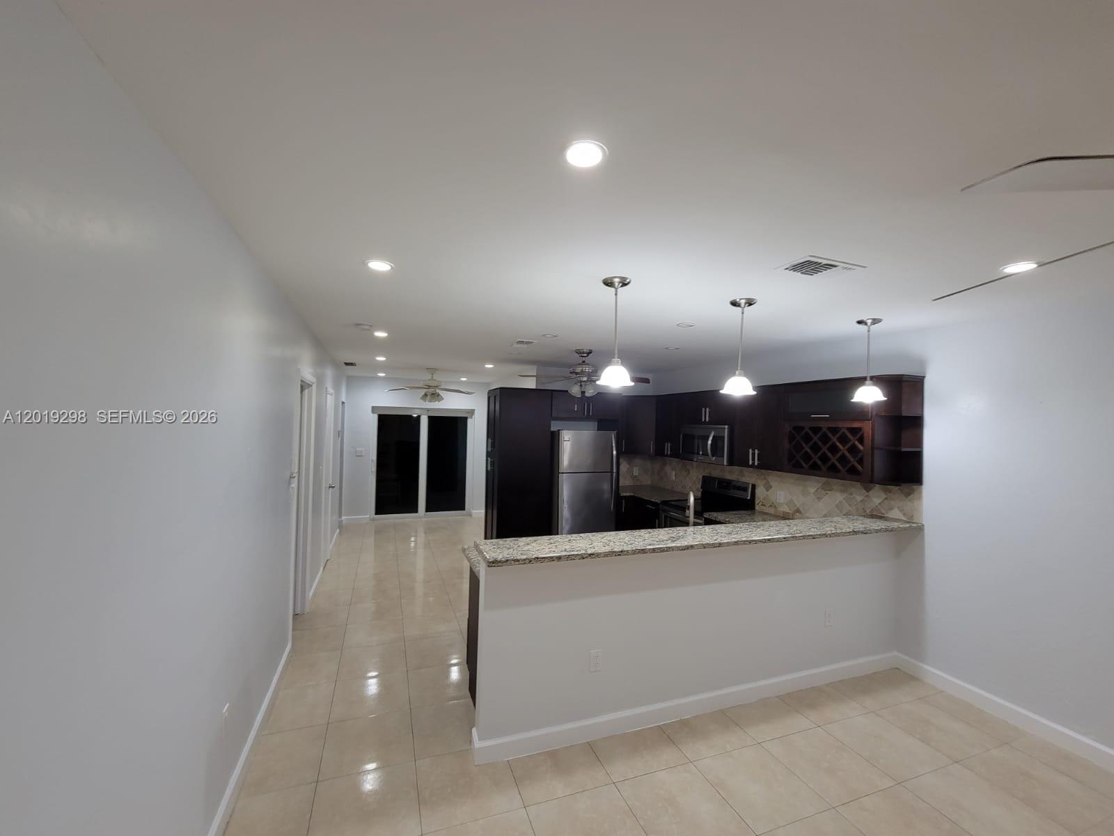 A kitchen with dark cabinets, granite countertops, and a breakfast bar overlooks a tiled room — 5780 SW 61st St # 5780, Miami FL 33143, MIAMI, FL
