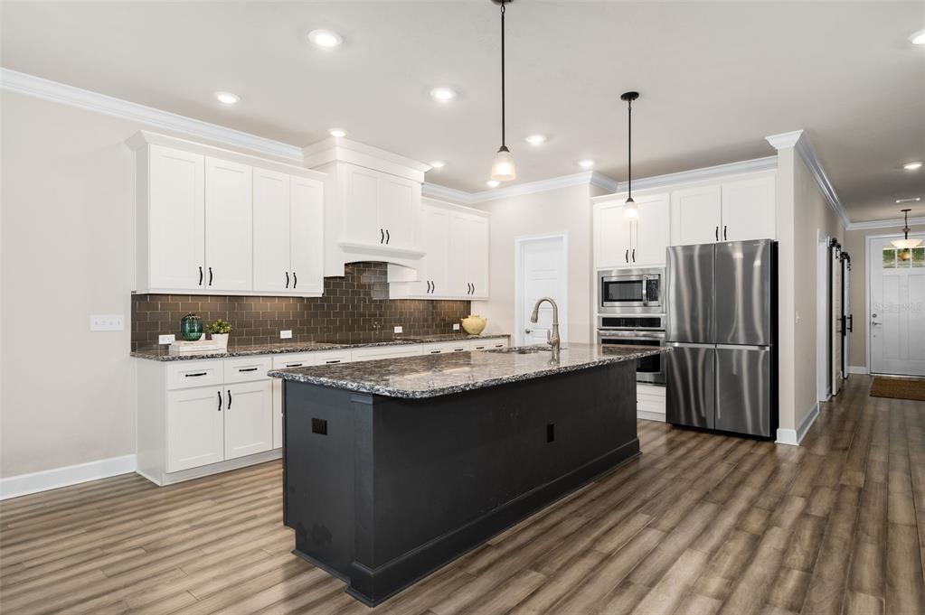 A kitchen features white cabinets, a dark island, granite countertops, and stainless steel appliances — 12926 SW 7TH AVENUE, NEWBERRY, FL