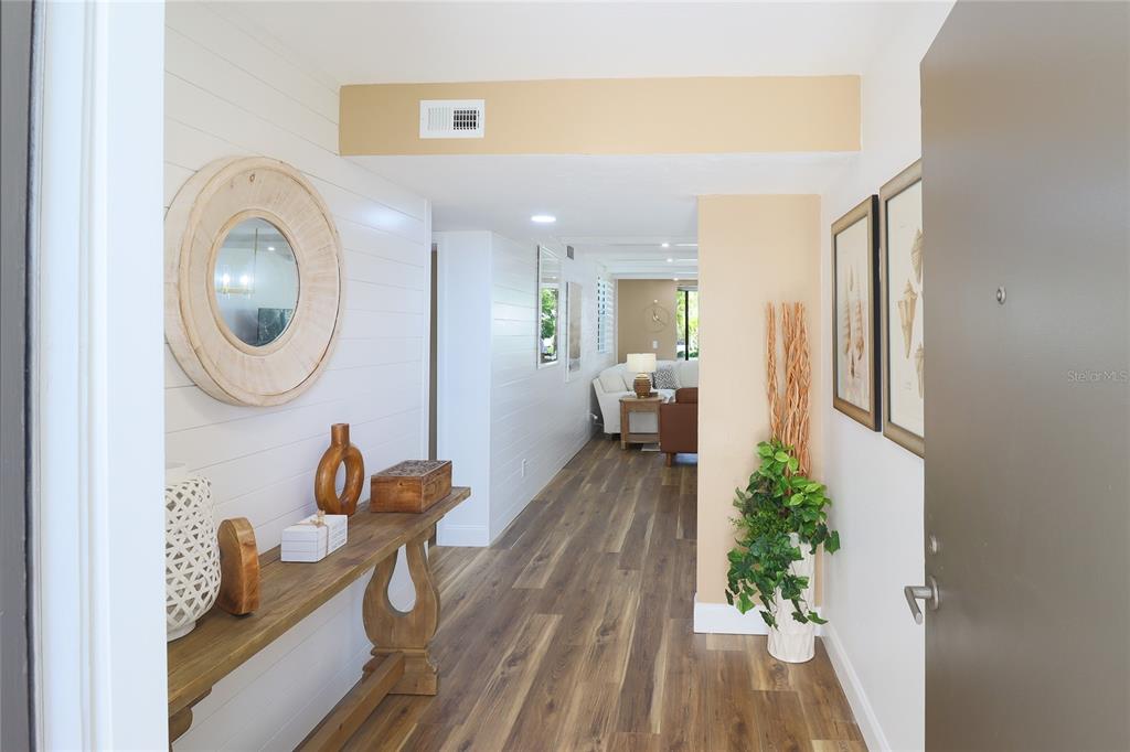 A hallway with wood-look flooring, shiplap walls, and a console table leads to a living area — 716 BAYPORT WAY UNIT 716, LONGBOAT KEY, FL