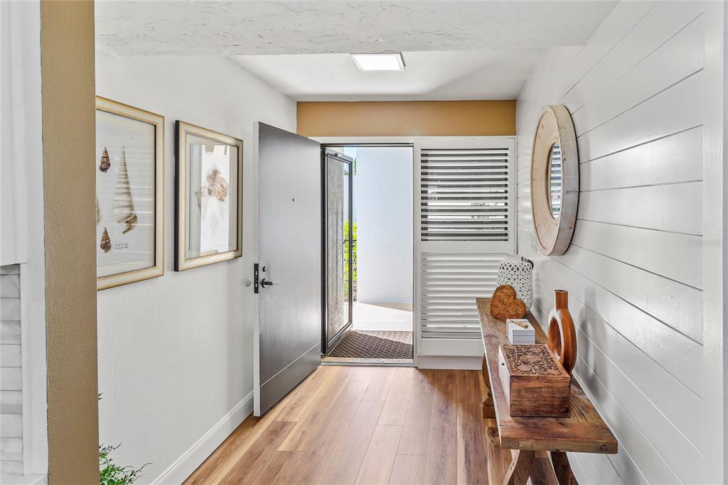 An entryway features wood-look flooring, white shiplap walls, a console table, and an open front door — 716 BAYPORT WAY UNIT 716, LONGBOAT KEY, FL