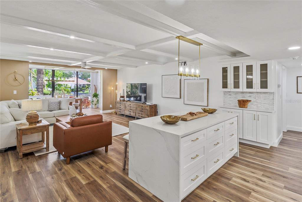 An open-concept living room and kitchen featuring a white island, wood flooring, and coffered ceilings — 716 BAYPORT WAY UNIT 716, LONGBOAT KEY, FL