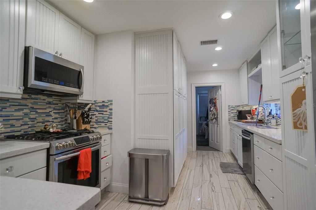 A galley kitchen features white cabinetry, stainless steel appliances, a tiled backsplash, and light-colored flooring — 328 CARL AVENUE, BELLEAIR, FL
