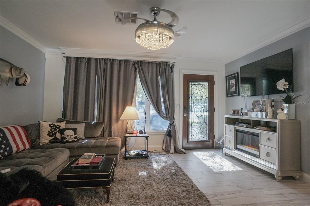 A living room features a grey sectional sofa, a crystal ceiling fan, and a fireplace console — 328 CARL AVENUE, BELLEAIR, FL