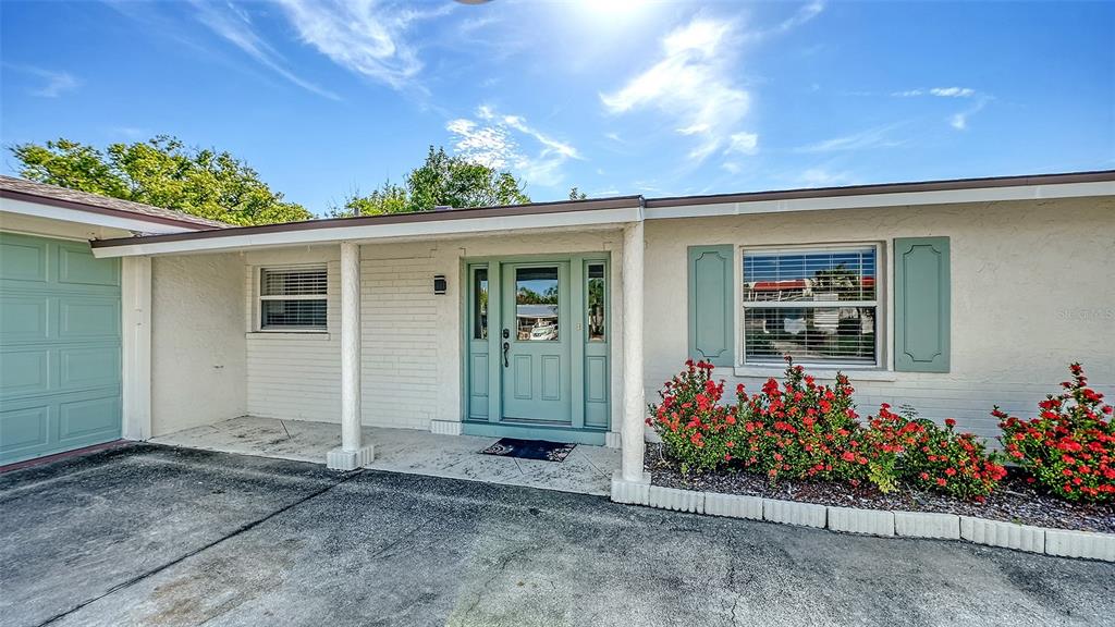 A single-story house exterior features a light-colored brick facade, a teal front door, and landscaping — 6515 COLONIAL DRIVE, SARASOTA, FL
