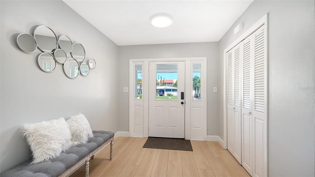 An entryway features light wood-look flooring, a gray bench, a cluster of mirrors, and white doors — 6515 COLONIAL DRIVE, SARASOTA, FL