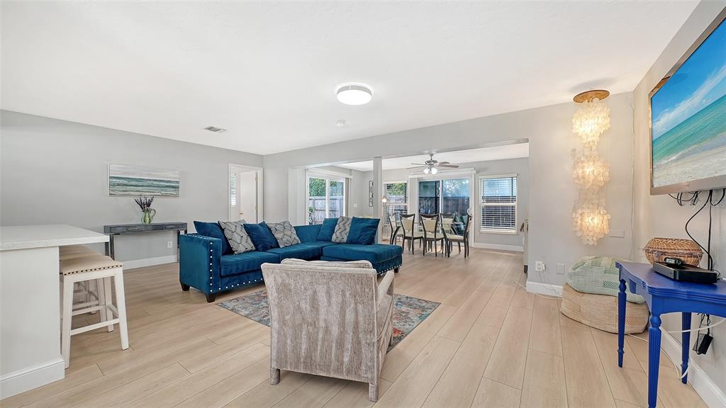 A living room with light wood floors, a blue sectional sofa, and a dining area — 6515 COLONIAL DRIVE, SARASOTA, FL
