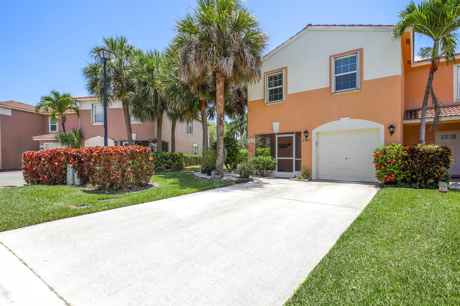 A two-story peach-colored townhouse features a concrete driveway, a garage, and palm trees — 6881 Willow Creek Run, FL 33463, FL