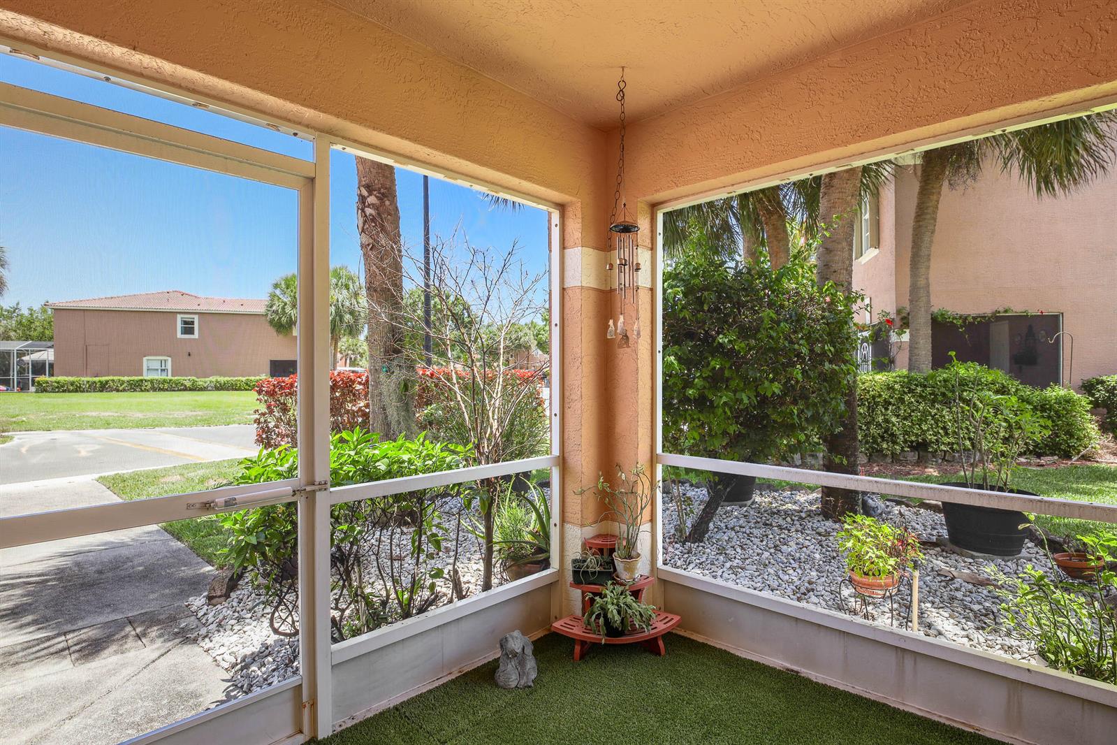 A screened-in porch features artificial turf flooring, a tiered plant stand, and views of landscaping — 6881 Willow Creek Run, FL 33463, FL