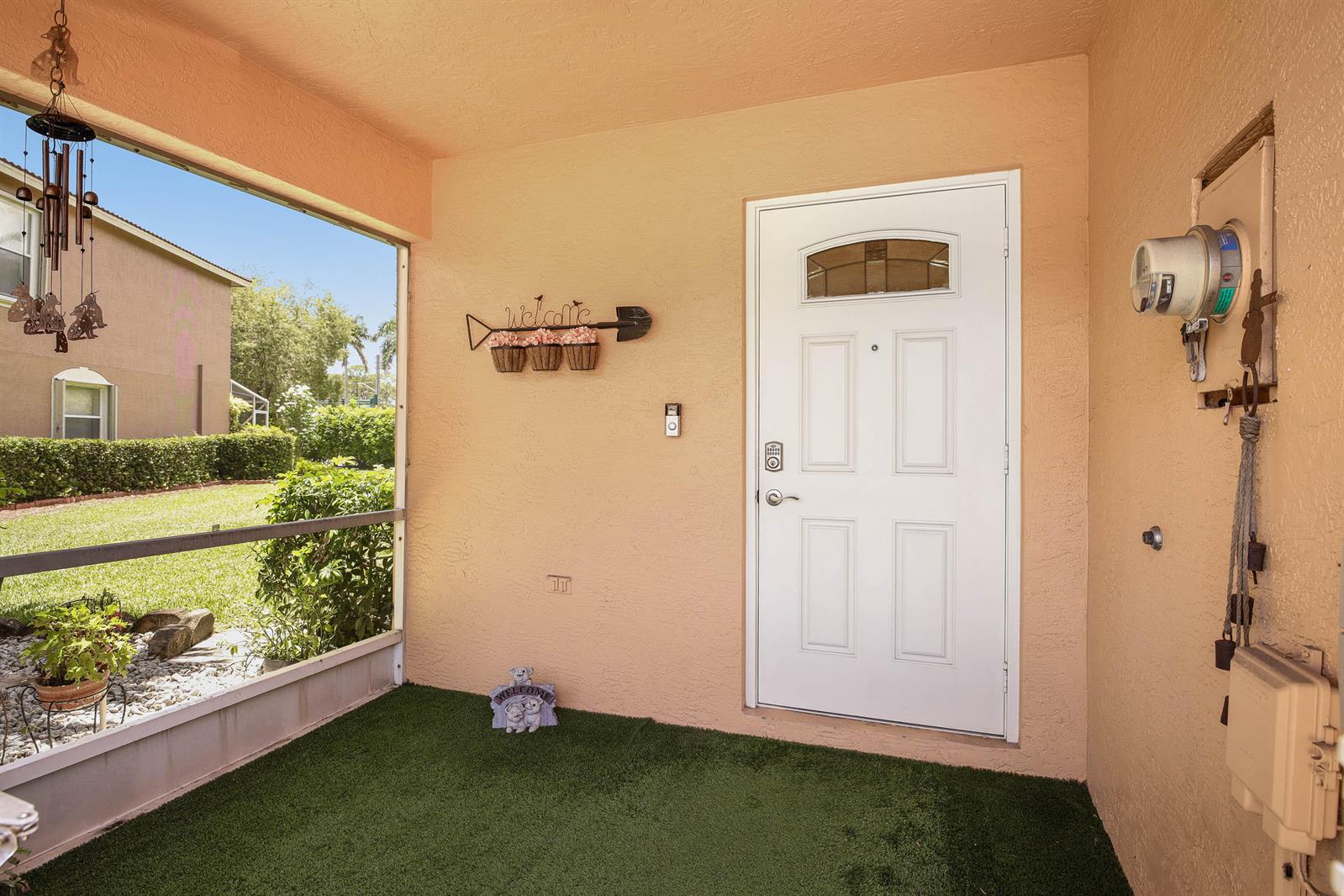 A covered entryway features a white front door, artificial turf flooring, and a decorative wall sign — 6881 Willow Creek Run, FL 33463, FL
