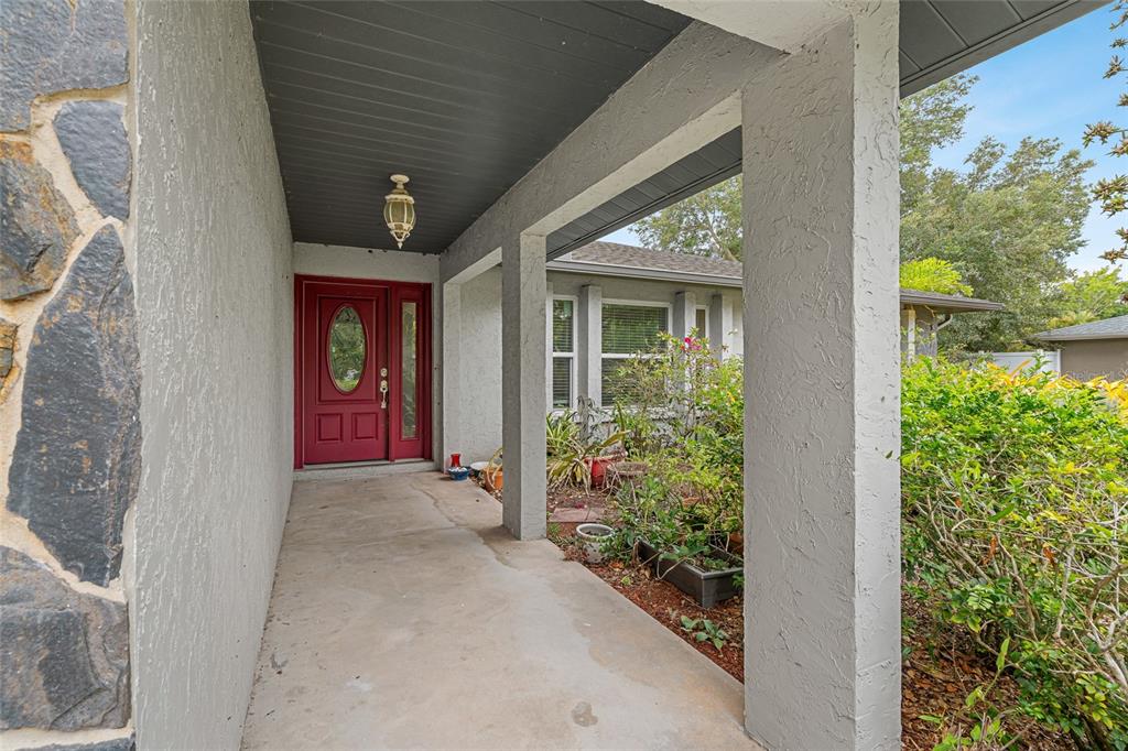 A covered concrete porch leads to a red front door with a glass oval insert — 4204 PRAIRIE VIEW DRIVE, SARASOTA, FL
