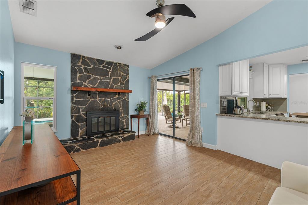 A living room with a stone fireplace, wood-look tile floors, and an open kitchen — 4204 PRAIRIE VIEW DRIVE, SARASOTA, FL