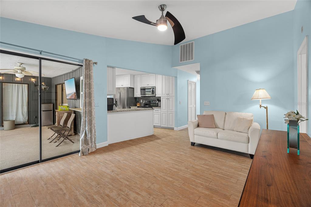 A living room with light blue walls, wood-look tile flooring, and an open kitchen view — 4204 PRAIRIE VIEW DRIVE, SARASOTA, FL