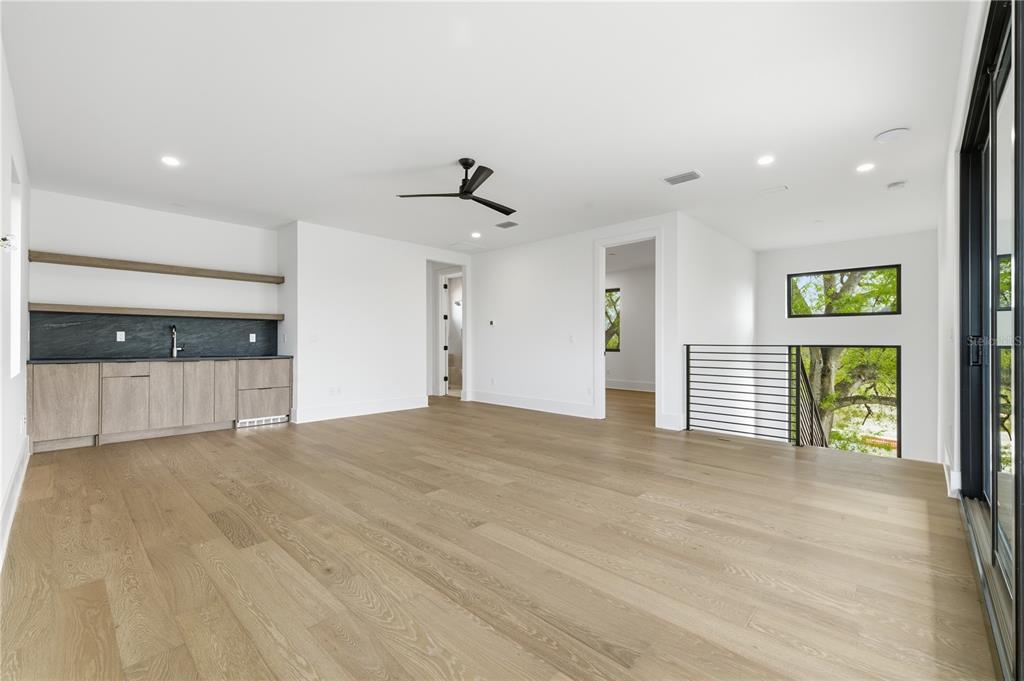 A modern room features light wood flooring, a wet bar with dark cabinetry, and a staircase — 2517 RIVERSIDE DR, TAMPA, FL