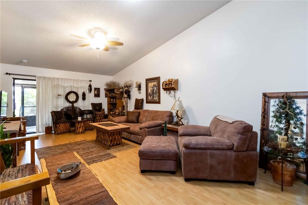 A living room features light wood flooring, brown upholstered furniture, and a vaulted ceiling — 6521 HERITAGE LANE UNIT 2621, BRADENTON, FL