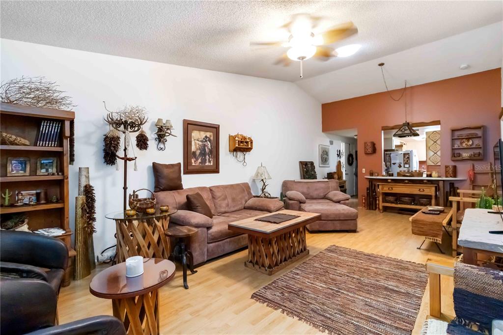 A living room features light wood flooring, a brown sofa, and a vaulted ceiling — 6521 HERITAGE LANE UNIT 2621, BRADENTON, FL