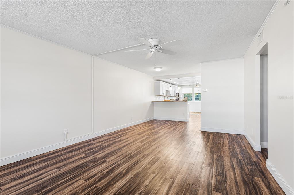 A living room with wood-look flooring, white walls, and a ceiling fan leads to a kitchen — 4915 BAY STREET NE UNIT 224, ST PETERSBURG, FL