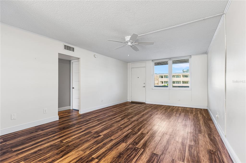 An empty room features wood-look flooring, a ceiling fan, white walls, and a large window — 4915 BAY STREET NE UNIT 224, ST PETERSBURG, FL