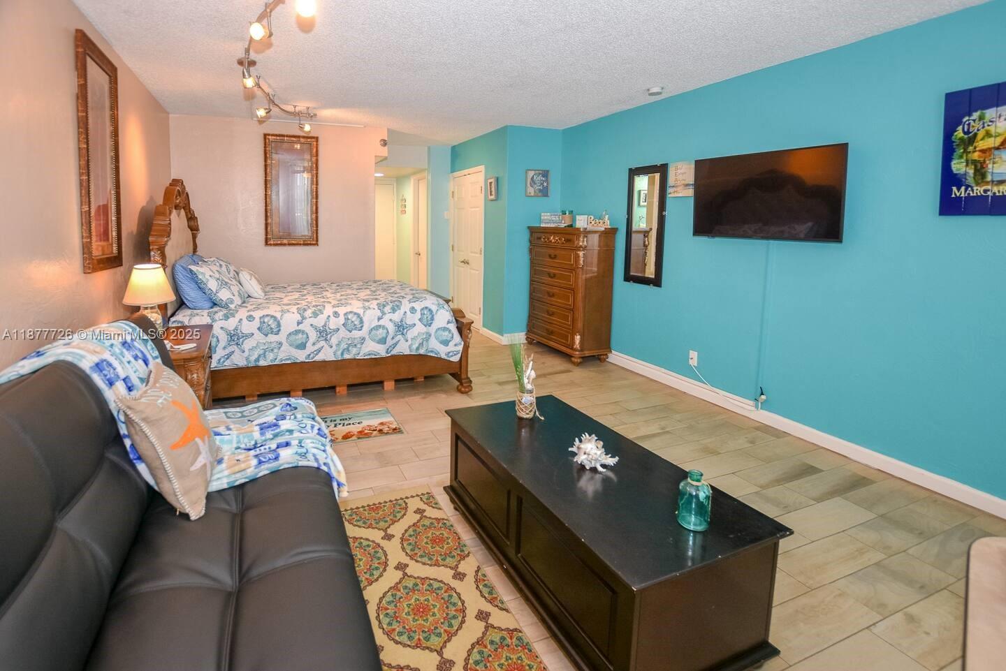 A bedroom with a bed, sofa, television, and dresser on a light-colored tiled floor — 313 S. ATLANTIC AVE # 217, Daytona FL 32118, DAYTONA, FL