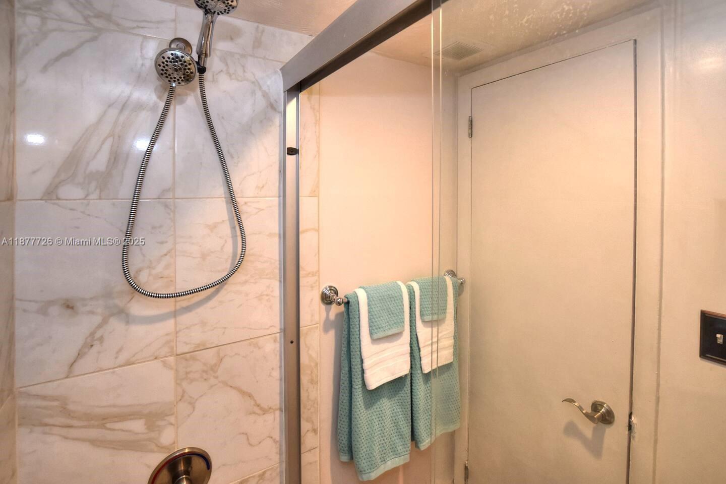 A shower with marble-patterned tile walls and a glass door features two hanging towels — 313 S. ATLANTIC AVE # 217, Daytona FL 32118, DAYTONA, FL