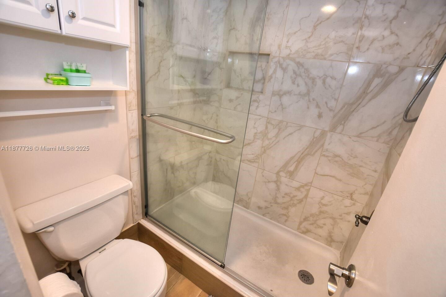 A bathroom features a white toilet, a glass-enclosed shower with marble-patterned tile, and wall shelving — 313 S. ATLANTIC AVE # 217, Daytona FL 32118, DAYTONA, FL