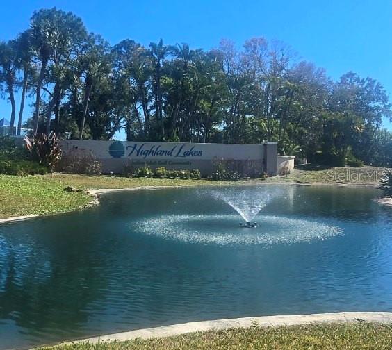 A pond with a fountain sits in front of a Highland Lakes community entrance sign — 1001 TARTAN DRIVE UNIT 302, PALM HARBOR, FL