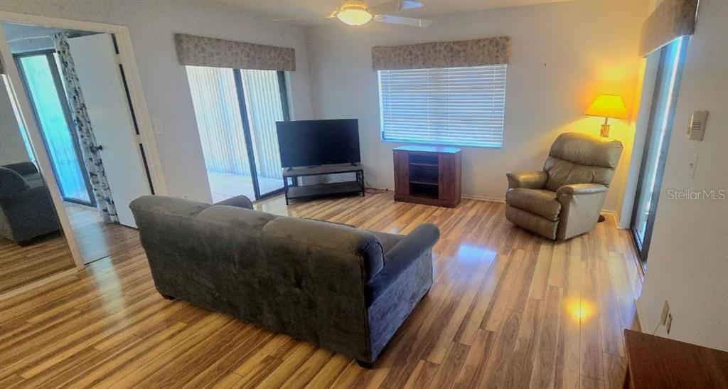 A living room features wood-look flooring, a gray sofa, a recliner, and a television stand — 1001 TARTAN DRIVE UNIT 302, PALM HARBOR, FL