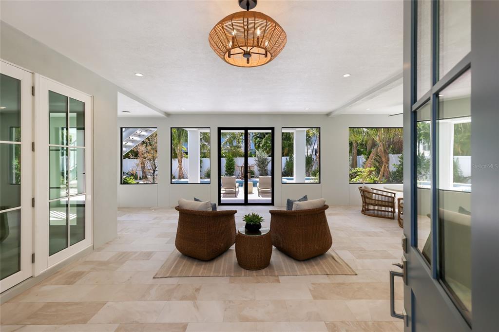 A bright, open-air patio features light tile flooring, wicker furniture, and views of a pool — 215 SYCAMORE AVENUE, ANNA MARIA, FL