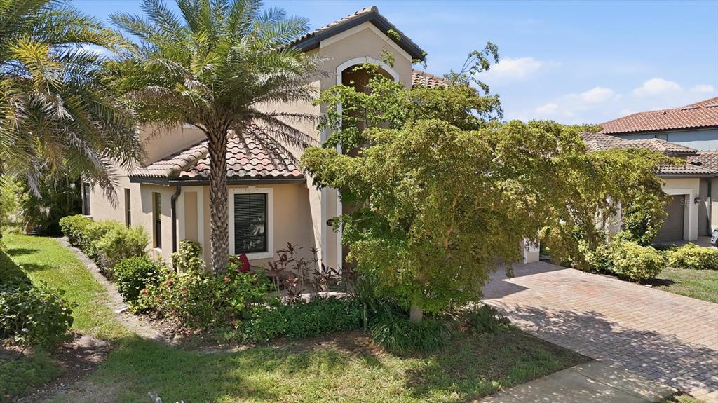 A two-story stucco house with a tile roof, palm tree, and brick paver driveway — 12505 CANAVESE LANE, VENICE, FL